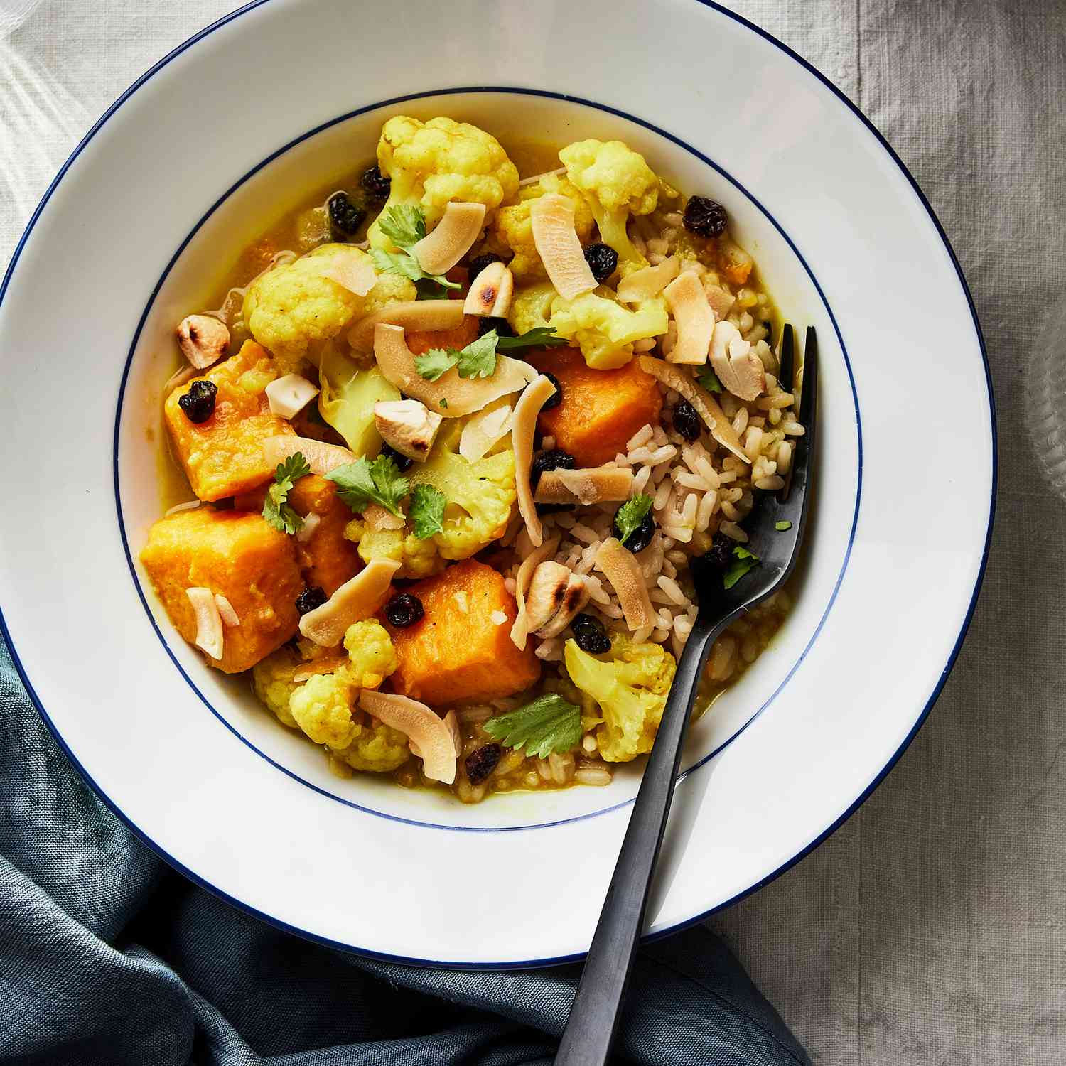 Foto de la receta de camote y coliflor al curry en olla de cocción lenta con coco y anacardos servidos en un tazón.