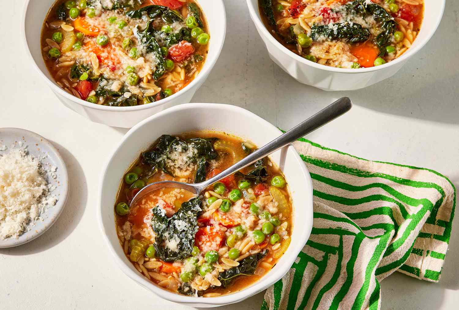 Tome 3 tazas de sopa de verduras desde un ángulo alto en un lugar brillante con lino a rayas.