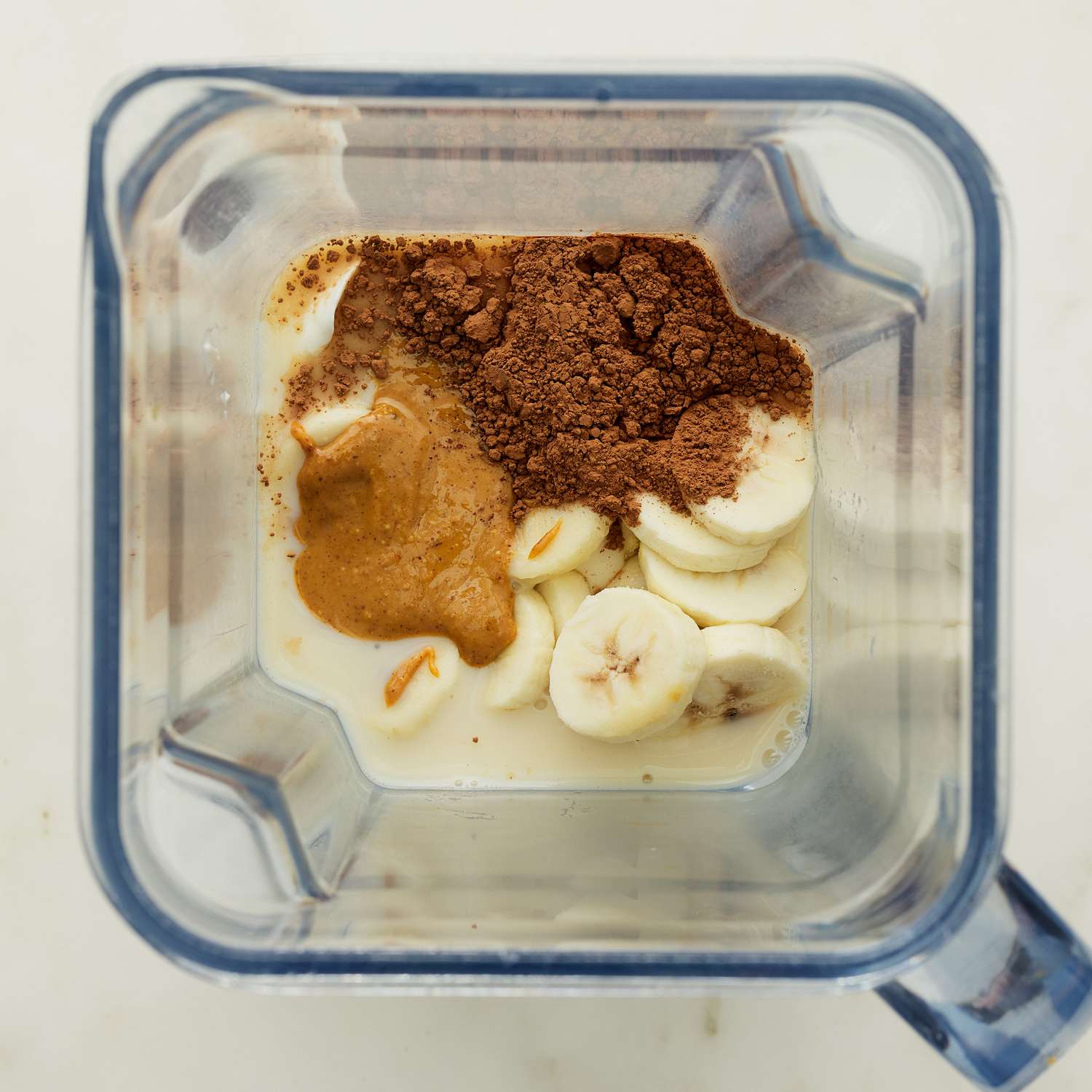 Sliza de plátano, mantequilla de maní y cacao en polvo para ver la parte superior de la licuadora llena de cacao en polvo