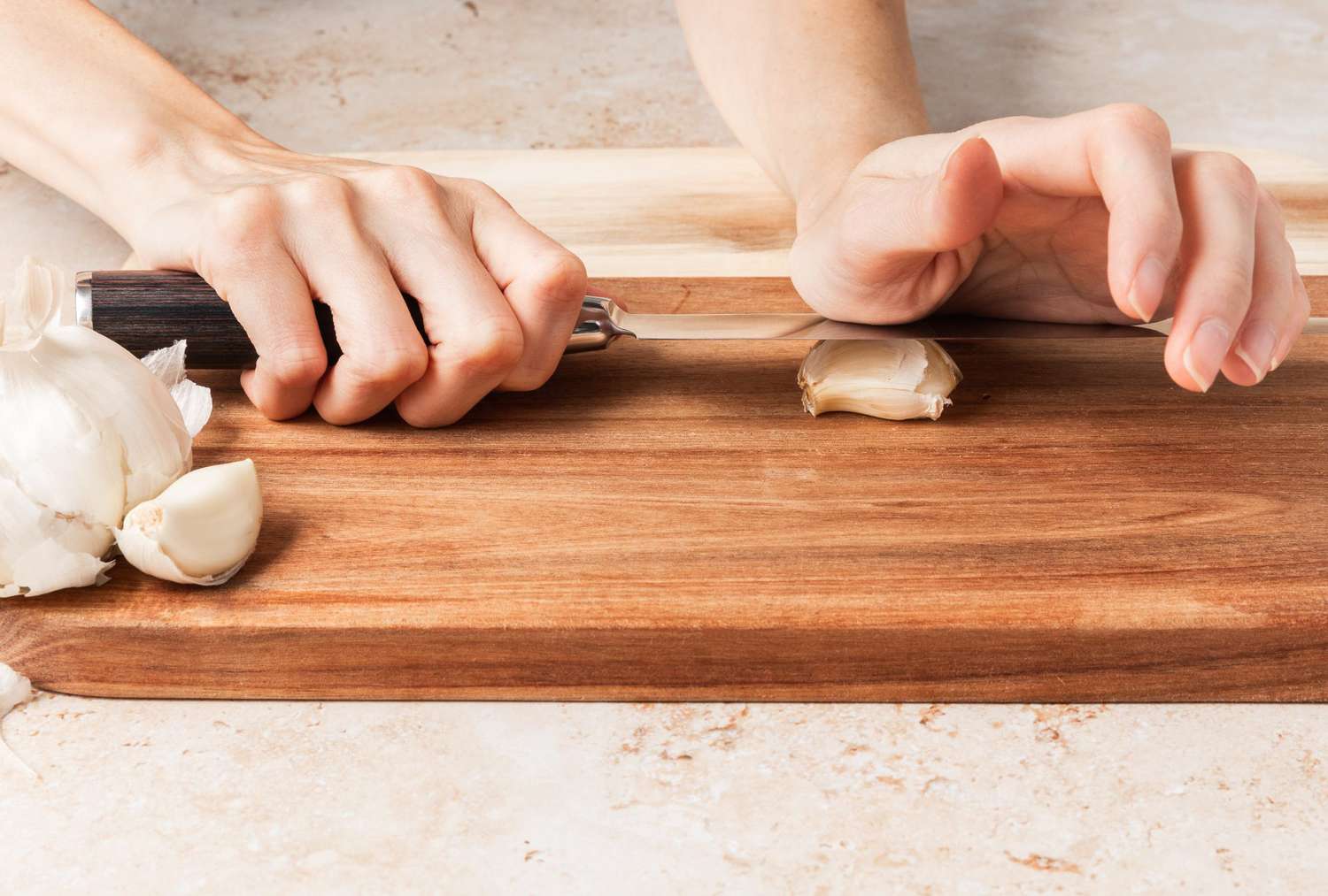 Foto de ángulo bajo de mano que sostiene el ajo con un cuchillo de cocina
