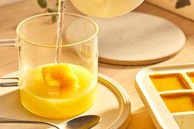 Una foto de receta con hielo en un frasco de jin de limón congelado y agua caliente se vierte en una taza.