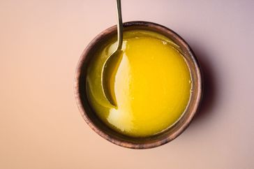 Foto de mantequilla clarificada en un recipiente de madera y una cuchara para revolverla.