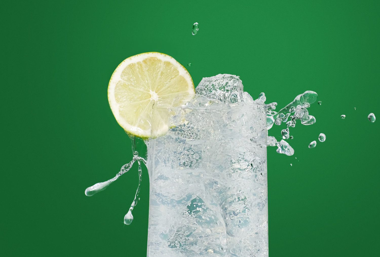 Foto de agua carbonatada vertida de un vaso con una rodaja de limón en el borde.