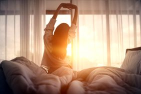 Foto de una mujer que se estira en la cama bajo el sol que ilumina el dormitorio