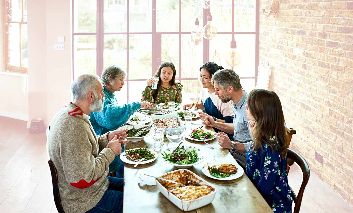 Un grupo mixto de parientes mayores sentados en una mesa, hablando y comiendo en un hogar relajado