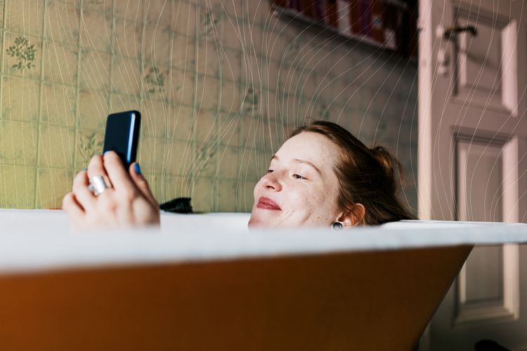 Una mujer sonriendo y enviando mensajes de texto mientras se baña