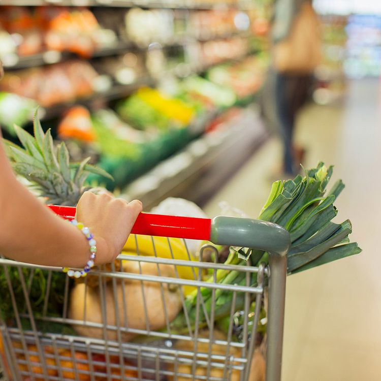 Mujer empujando un carrito de compras lleno de comida saludable