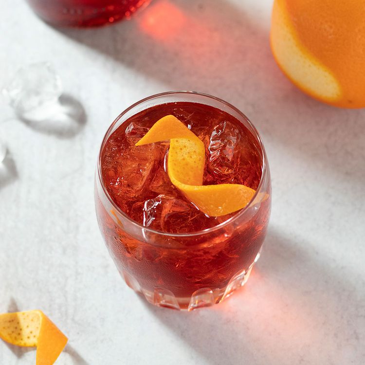 Un clásico Negroni borracho en un vaso con cáscara de naranja sobre un fondo blanco.