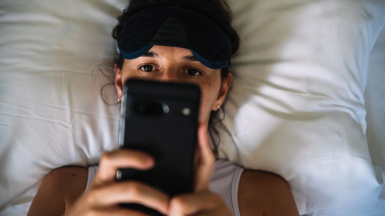 Una mujer mirando un teléfono inteligente en la cama.