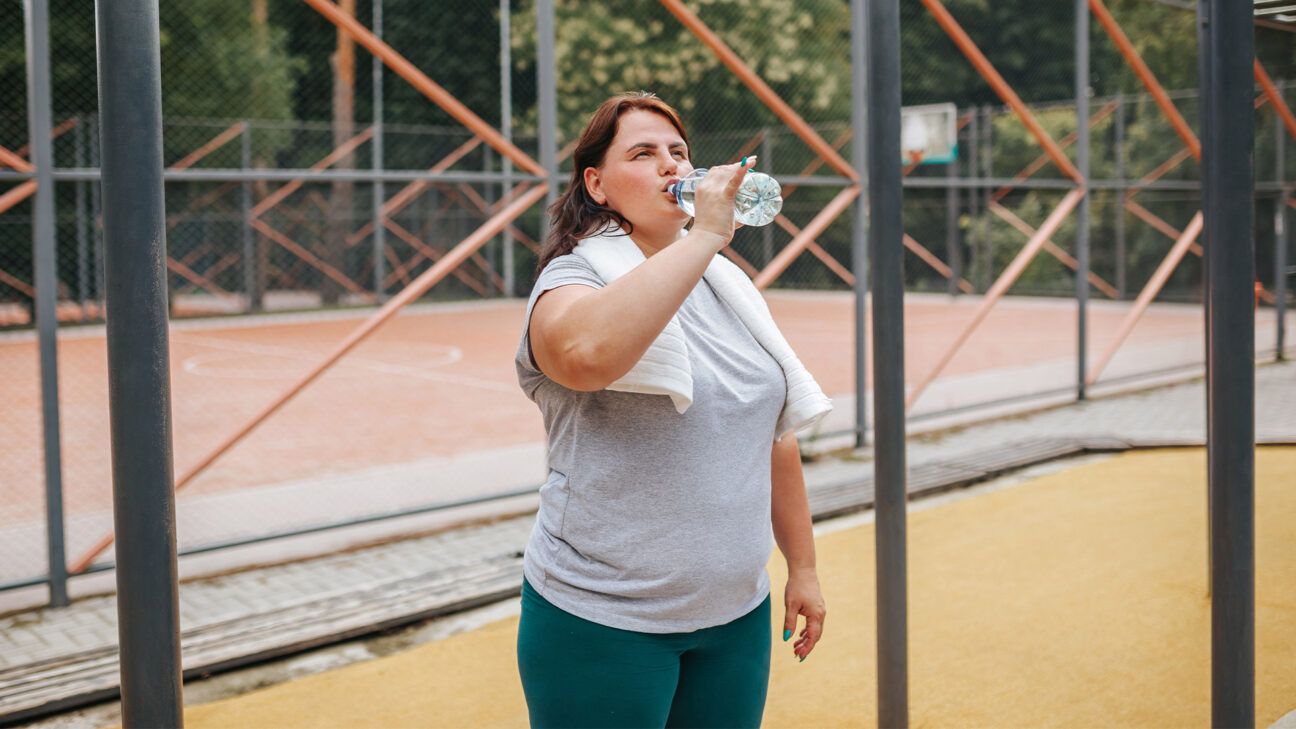 Una mujer que bebe agua en una botella de agua con un abrigo de baloncesto al aire libre < Span>, 