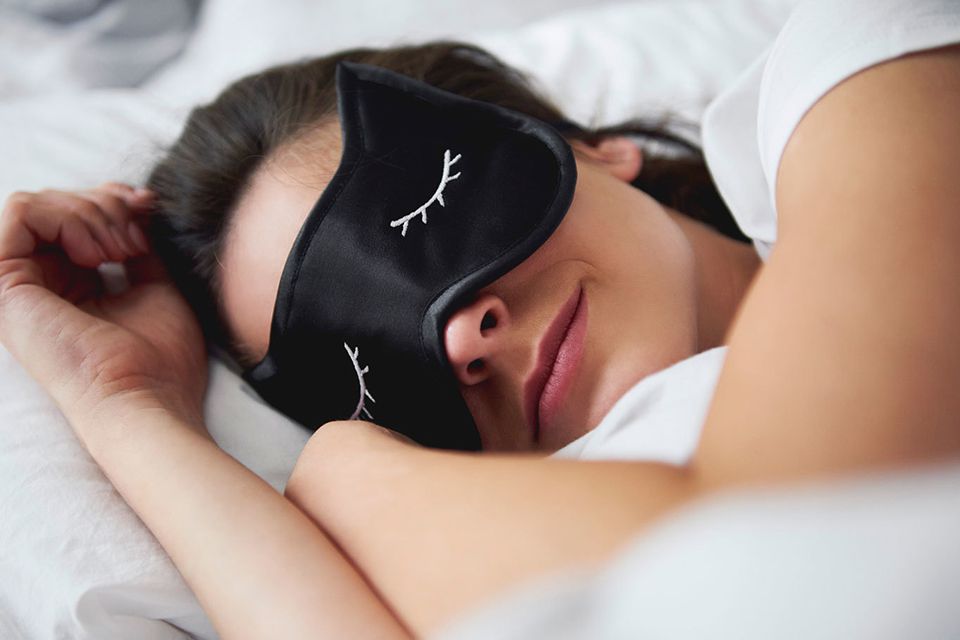 Una mujer acostada en la cama con una máscara de sueño