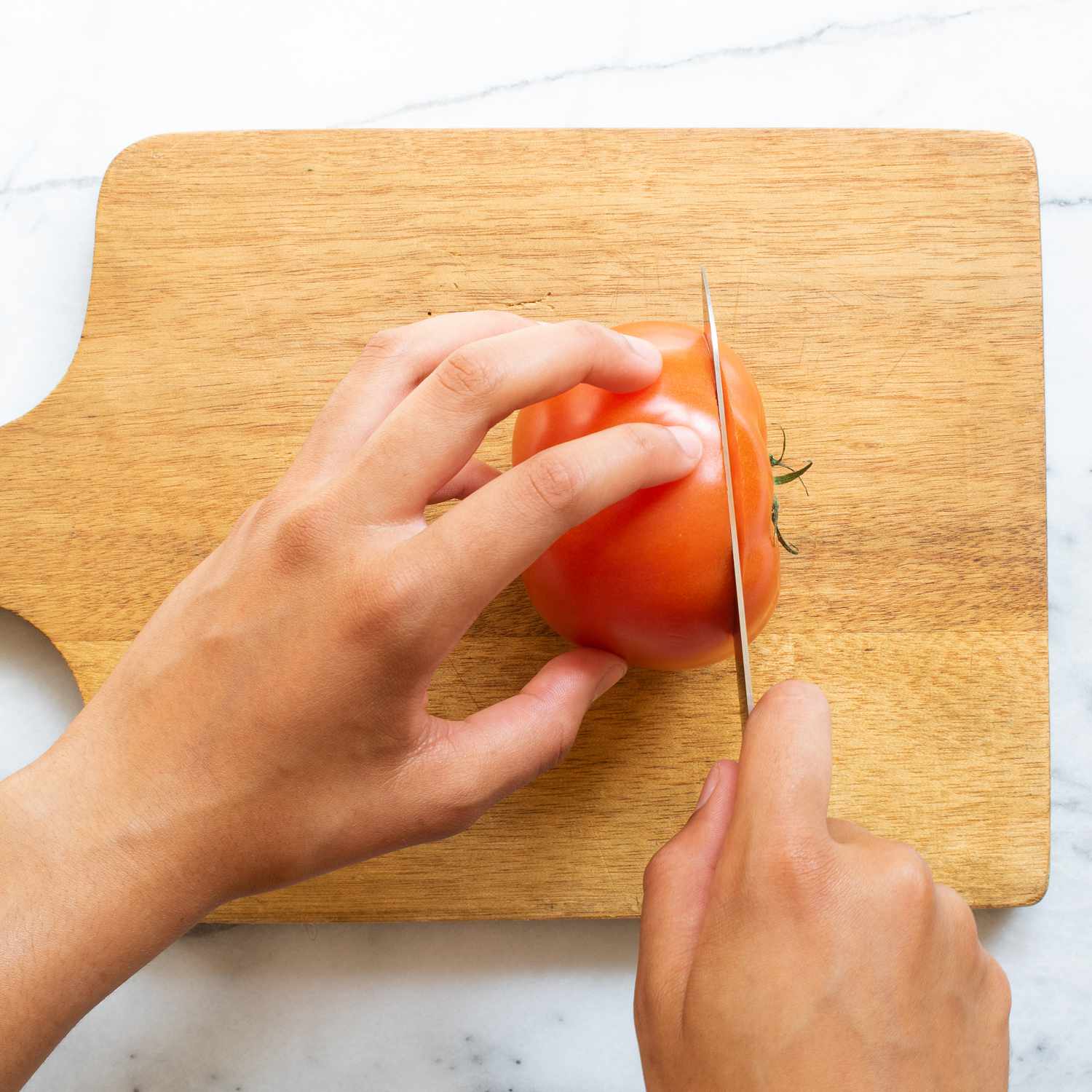 Mano usando un cuchillo para cortar tomates en una tabla de cortar de madera