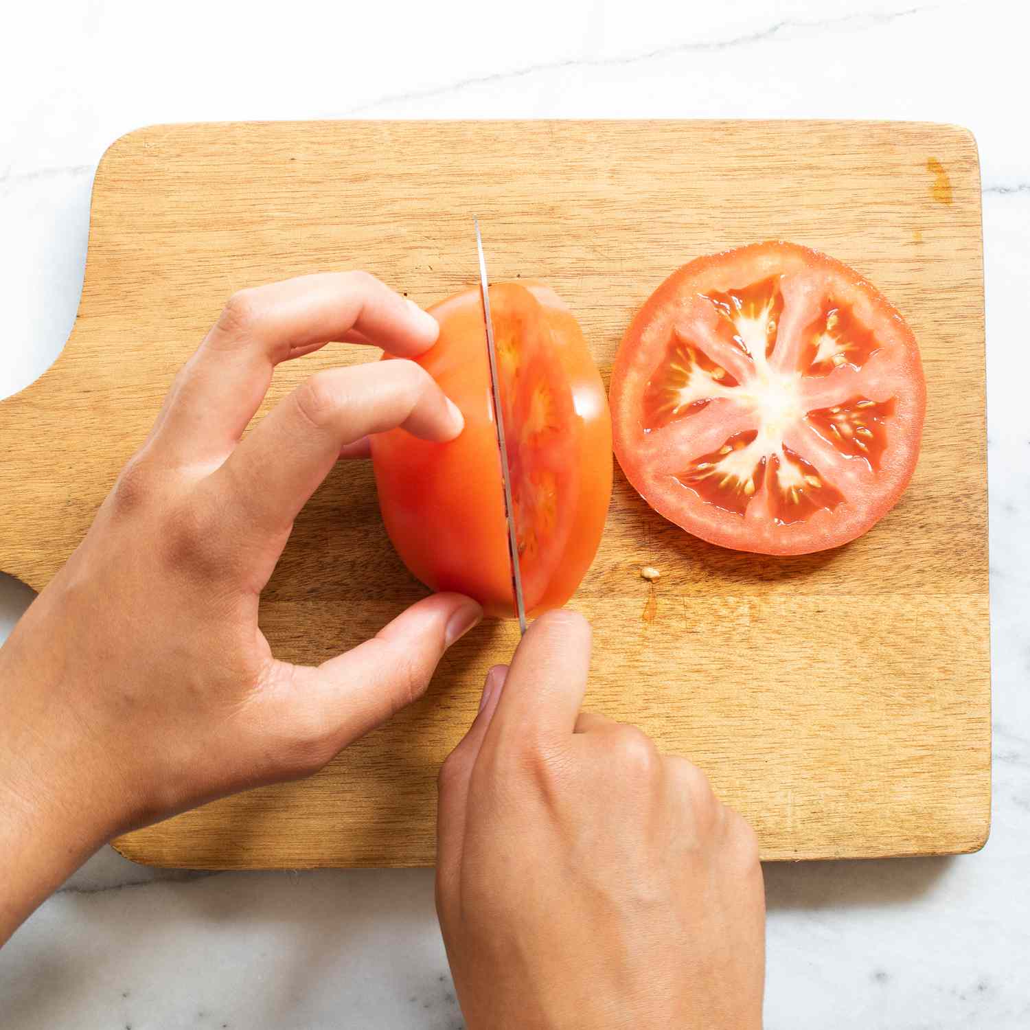 Mano usando un cuchillo para cortar tomates en una tabla para cortar