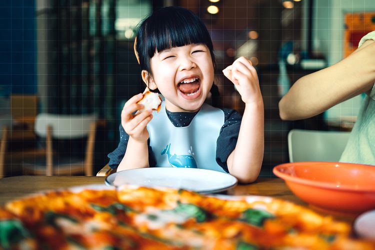 Una niña sentada a la mesa y comiendo felizmente.