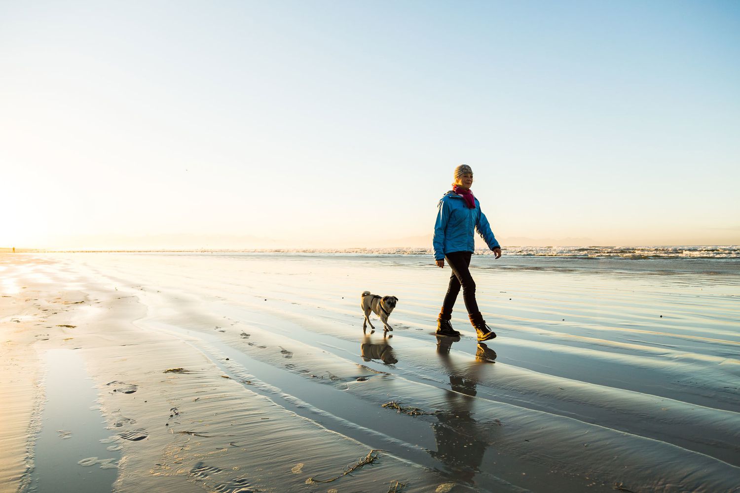 Mujer paseando con perro en la playa.