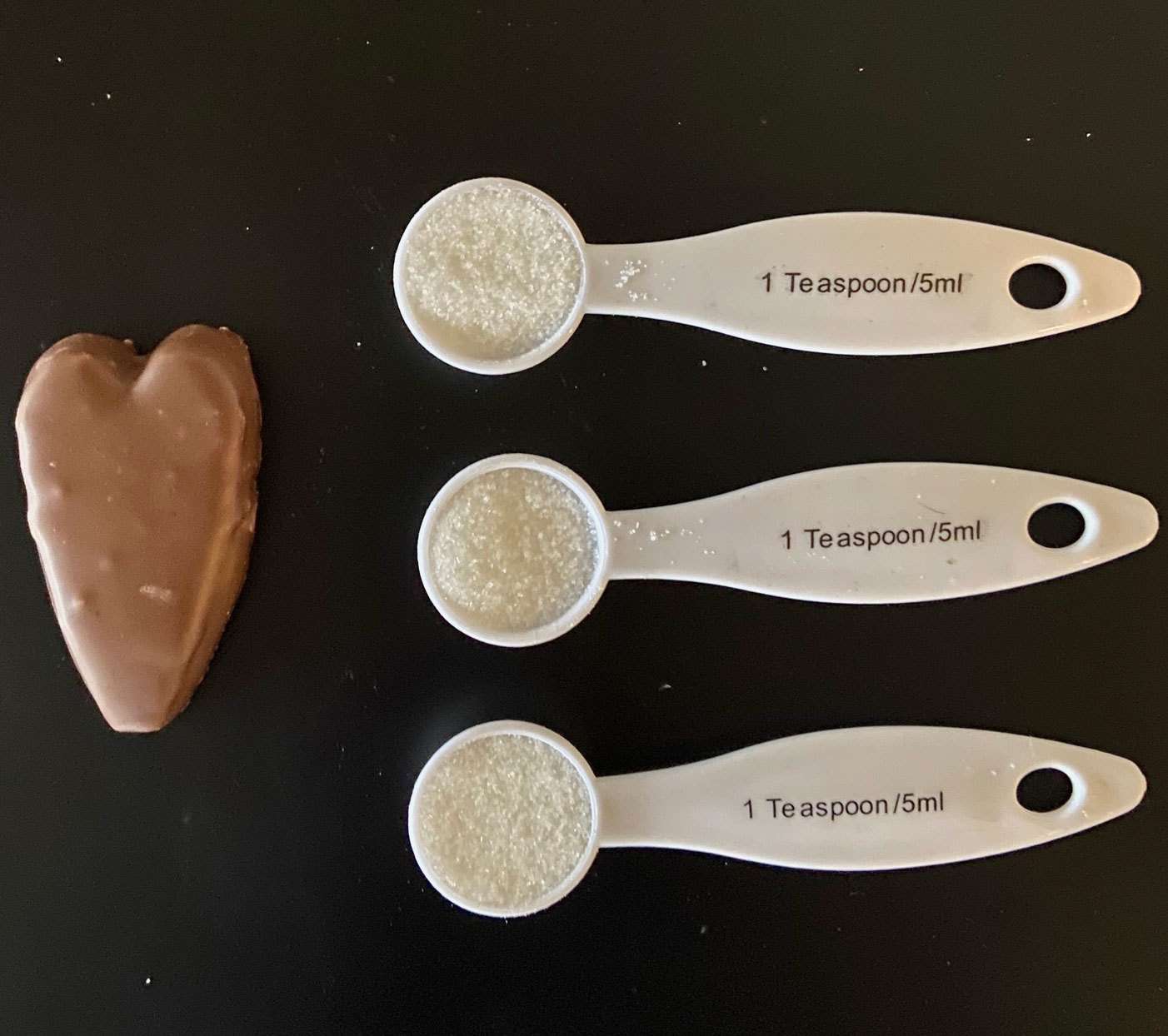 Tres cucharadas de azúcar con un corazón en forma de corona y una cuchara medidora al lado