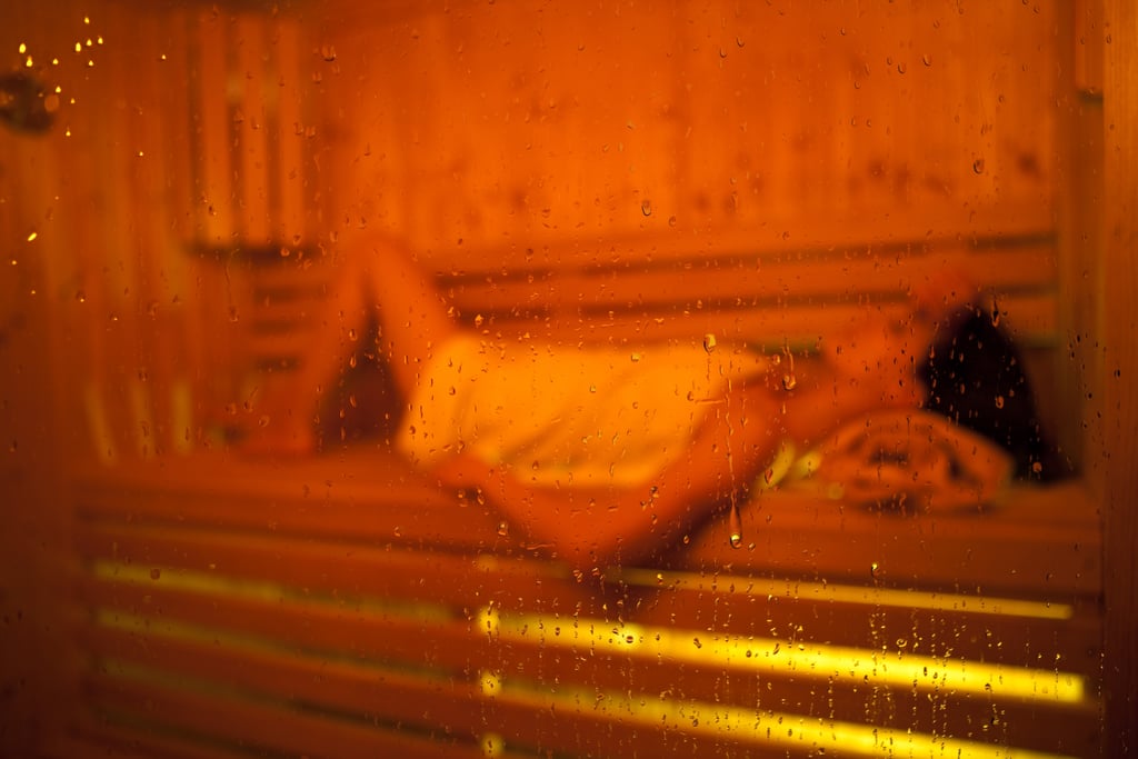 La niña en la sauna recibió un disparo a través del vaso de la sauna de vidrio. Concéntrese en las gotas de agua en la puerta.