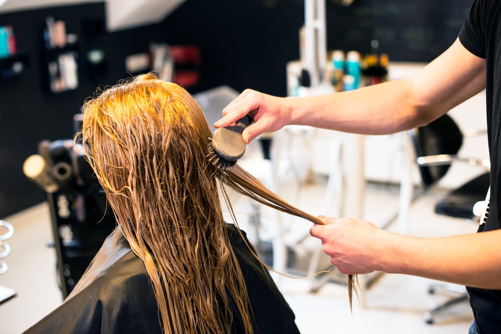 Un peluquero que cepilla el cabello de una mujer joven