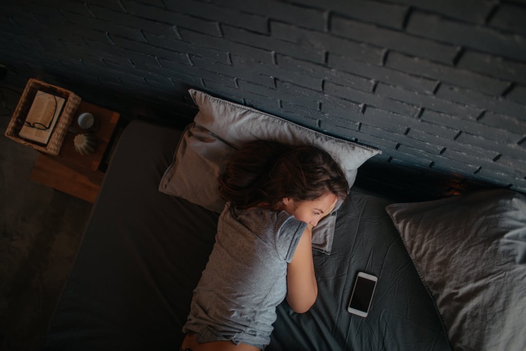 Foto de una mujer joven acostada en la cama esperando una llamada en su teléfono móvil