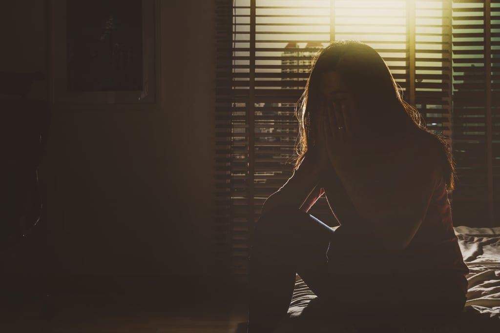 Mujer deprimida sentada boca abajo en un dormitorio oscuro.