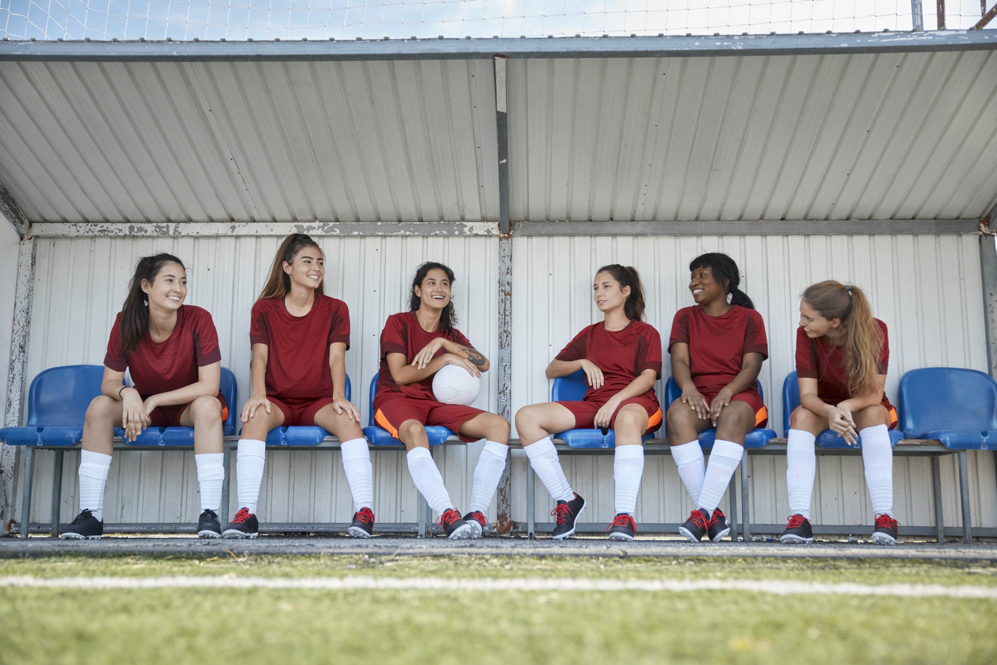Un grupo de adolescentes multiétnicos se sientan en el banco y conversan después de una práctica de fútbol.