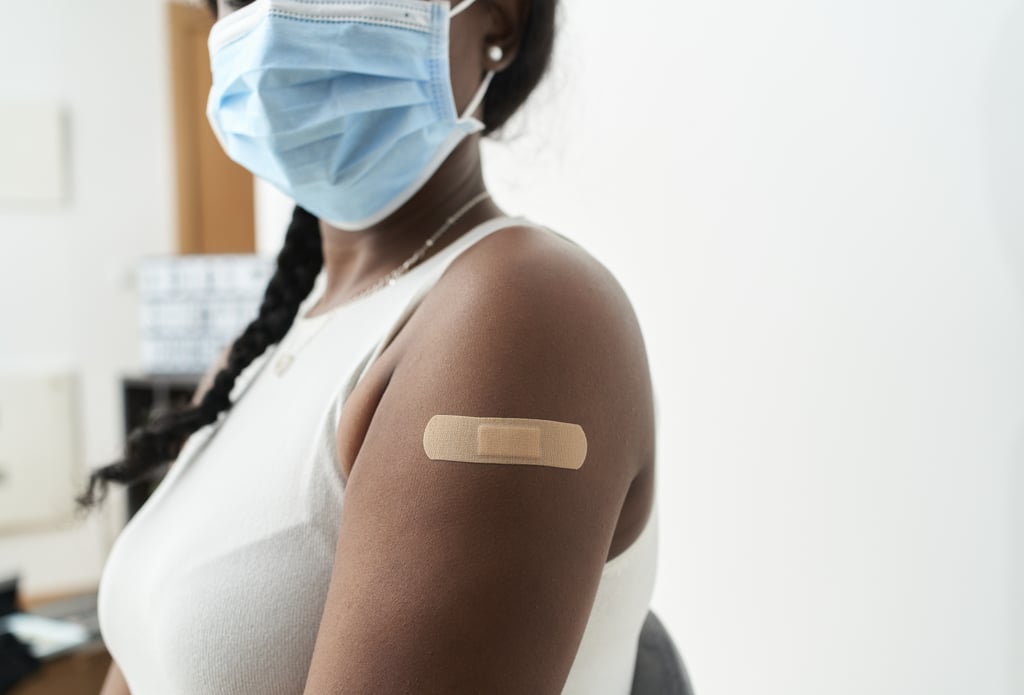Una mujer negra con el pelo trenzado, una camisa blanca y una mascarilla muestra una banda en la mano después de vacunarse. Conceptos de Covid