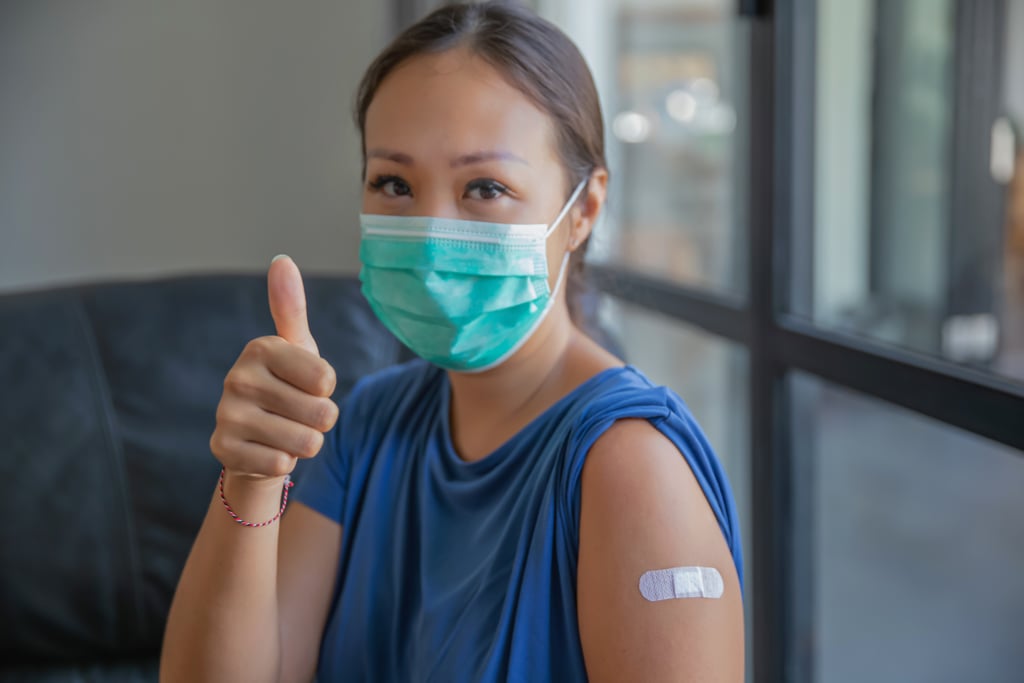 Primer plano de una orgullosa mujer asiática con una máscara protectora y levantando el pulgar después de recibir la vacuna COVID-19 en una clínica. Ella