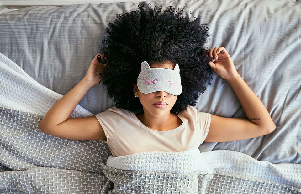 Una mujer acostada en la cama con una máscara para dormir sobre los ojos